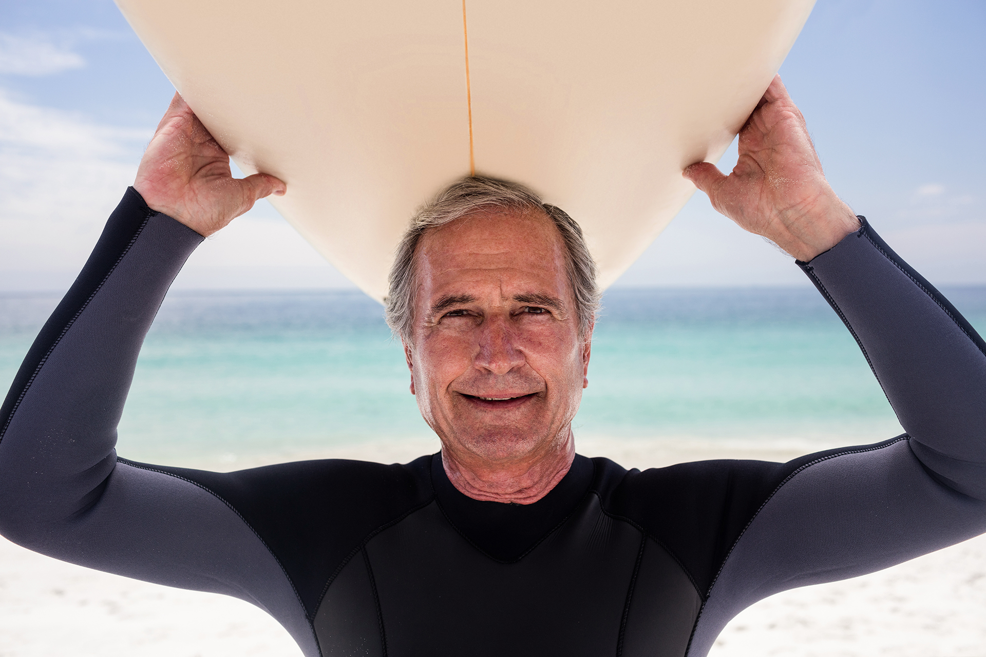 Portrait of senior man holding a surfboard over his head on the beach
